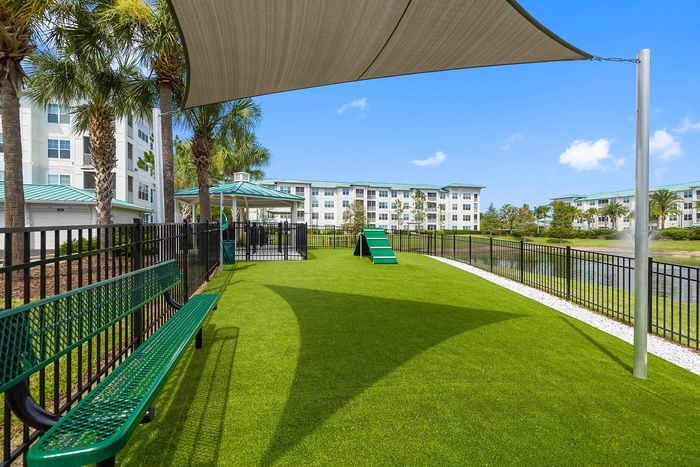 Inviting community area with lush green lawns, shaded seating, and a scenic view of modern apartment buildings and tranquil water features.