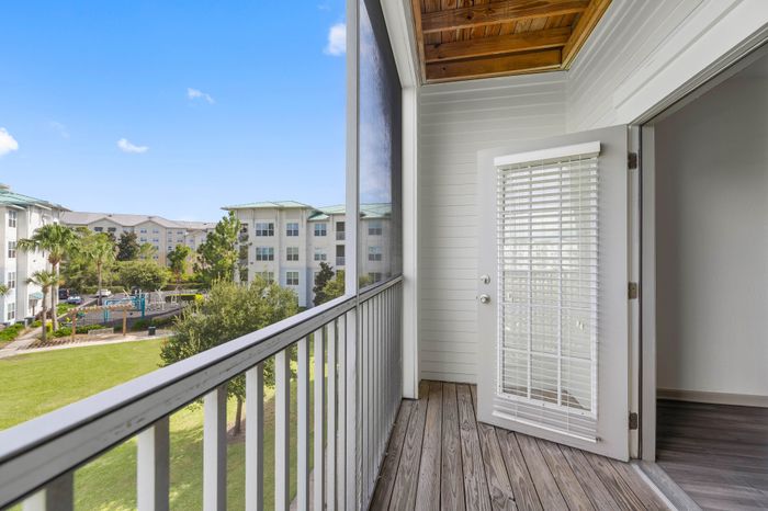 Inviting balcony view showcasing lush green courtyard and elegant multi-story apartments under a clear blue sky.