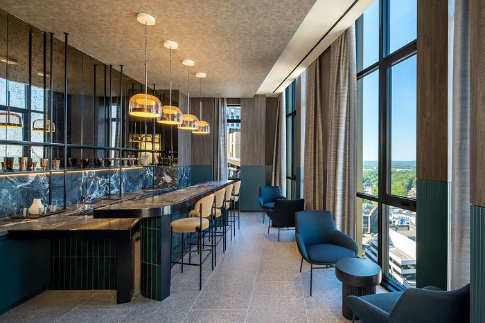 Elegant lounge area with marble-topped bar, stylish seating, pendant lighting, and expansive windows offering a panoramic city view.