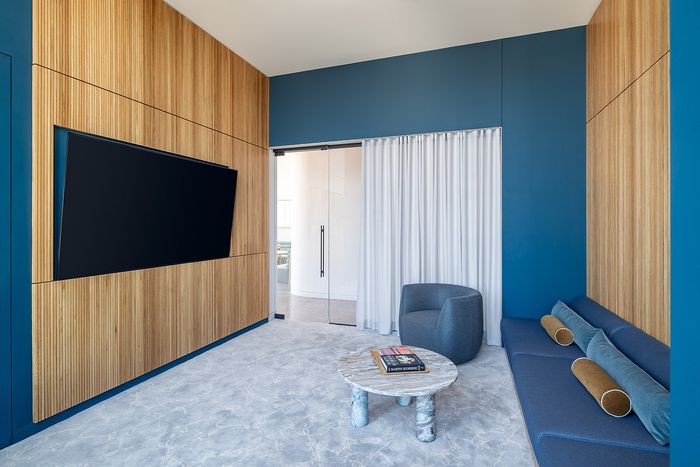 Modern living space with sleek wooden paneling, a stylish blue accent wall, plush seating, and elegant marble table.
