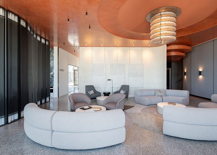 Elegant and modern lounge area featuring curved gray sofas, chic armchairs, and contemporary lighting under a stylish orange ceiling.