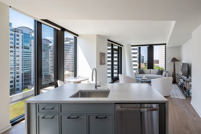 Modern city apartment with sleek kitchen island, floor-to-ceiling windows, and a cozy living area offering stunning urban views.