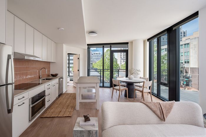 Modern open-concept living area with sleek kitchen, elegant dining space, and large windows offering city views.