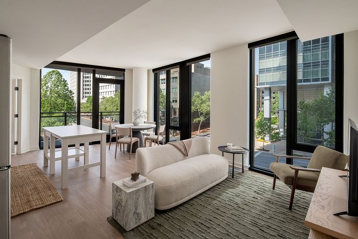 Modern living space with floor-to-ceiling windows, sleek furniture, and a cozy dining area overlooking an urban landscape.