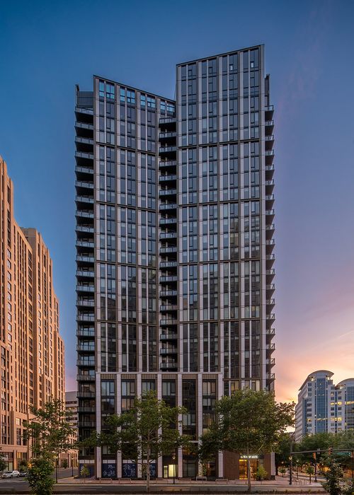 Modern high-rise building with sleek glass facade and stunning sunset backdrop, offering urban luxury living.