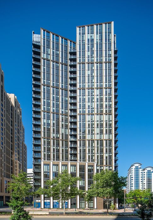 Sleek urban high-rise apartment building with modern design and expansive windows, set against a clear blue sky.