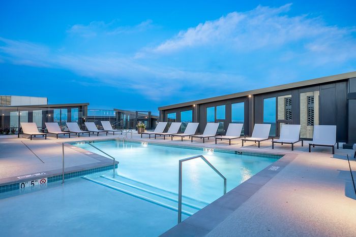 Modern apartment rooftop pool with stylish lounge chairs, expansive city views, and a vibrant sunset backdrop.