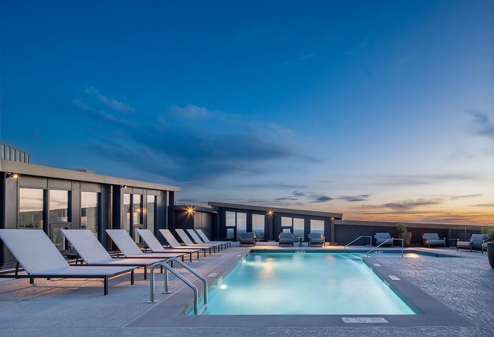 Luxurious rooftop pool with modern lounge chairs and stunning sunset view, perfect for relaxation and leisure.