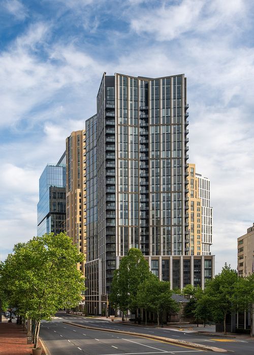 Modern high-rise apartment building with sleek design and expansive glass windows, set against a vibrant city backdrop.