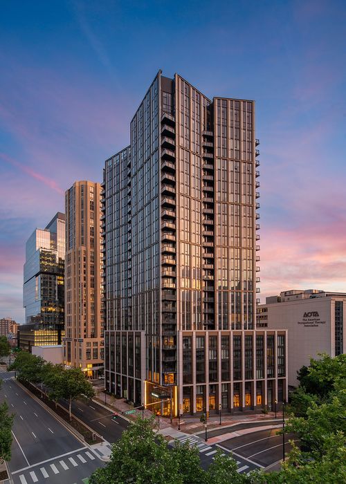 Modern high-rise apartment building with sleek glass fa&ccedil;ade and sunset reflection, set in a vibrant urban location.