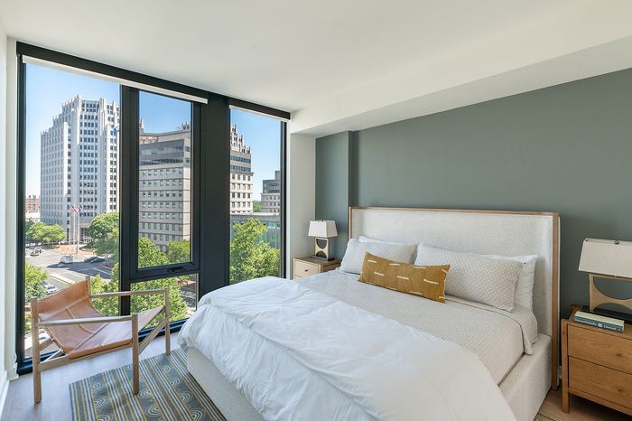 Chic urban bedroom with a plush bed, modern decor, and stunning city views through expansive windows.