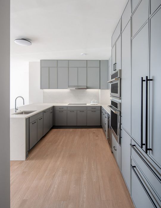 Modern kitchen with sleek gray cabinetry, integrated appliances, and elegant light wood flooring.