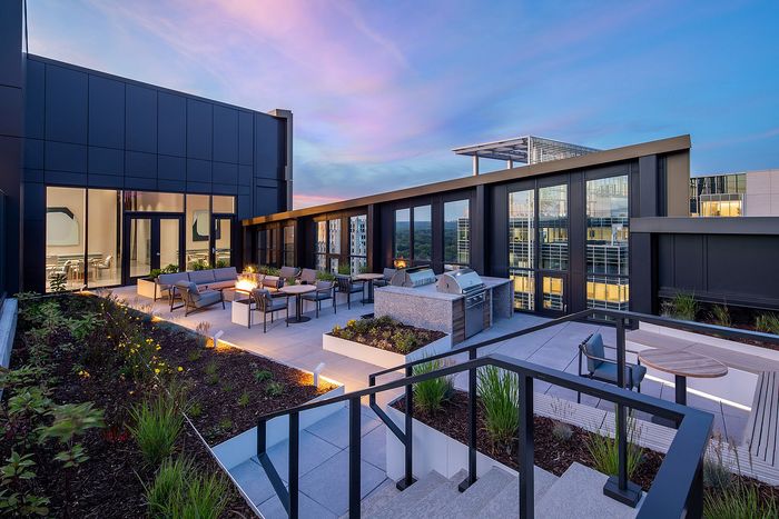 Luxurious rooftop terrace with cozy seating, fire pit, and modern outdoor kitchen, set against a stunning sunset skyline.