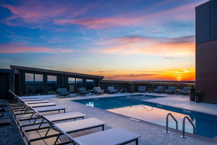 Luxurious rooftop pool area with stylish lounge chairs set against a breathtaking sunset sky, offering an idyllic retreat.