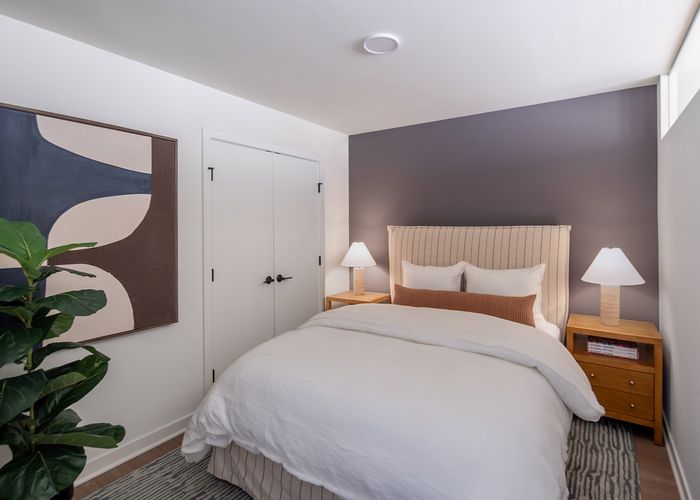 Cozy bedroom featuring a plush bed with elegant bedding, stylish end tables with soft lighting, and a chic abstract art piece on the wall.