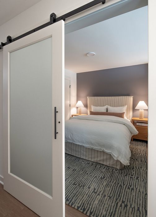 Cozy bedroom with an elegant sliding barn door, featuring a plush bed with neutral tones and inviting ambient lighting.