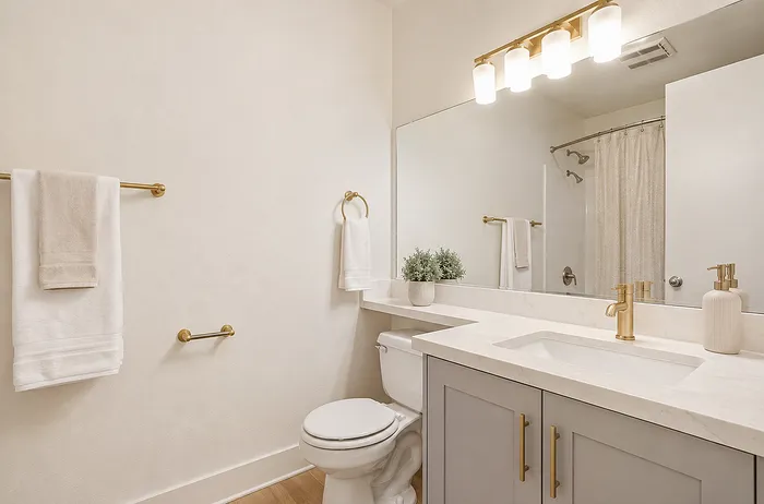 Elegant bathroom with modern fixtures, featuring a large mirror, white countertop, and gold accents for a luxury feel.