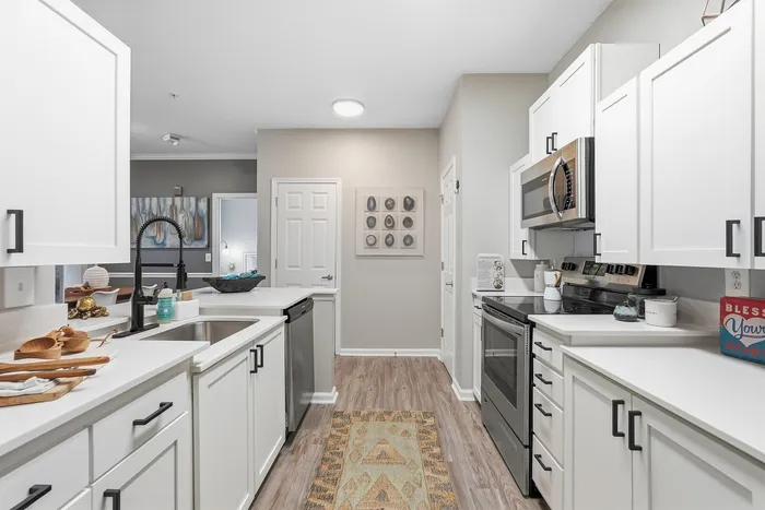 Modern, sleek kitchen with white cabinetry, stainless steel appliances, and elegant wood flooring, offering a bright and inviting cooking space.