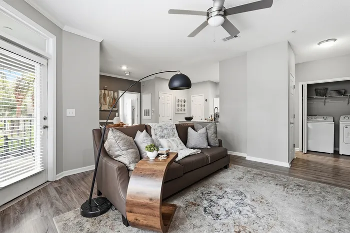 Modern living room with elegant decor, featuring a cozy brown sofa, stylish floor lamp, and a view of a bright balcony through large windows.