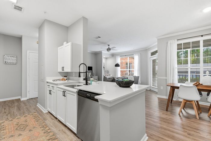 Modern open-concept living area showcasing sleek kitchen with white cabinets, stainless steel appliances, and inviting dining space filled with natural light.