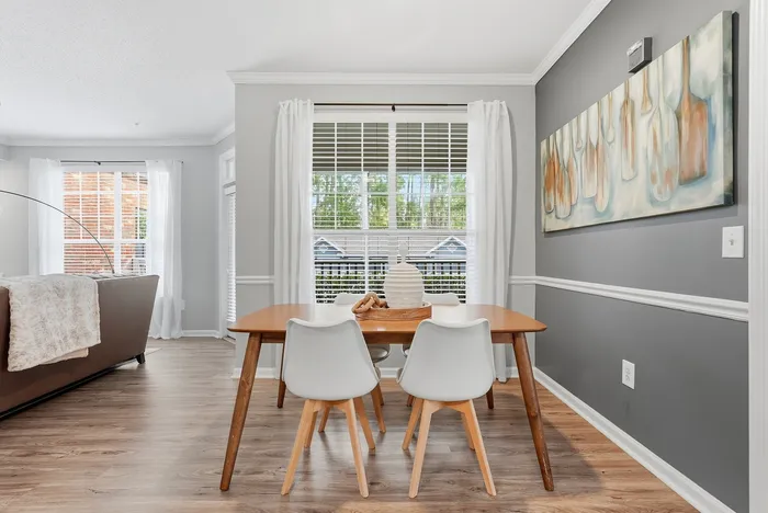 Bright and inviting dining area with modern wooden table, white chairs, and large windows framed by elegant curtains.