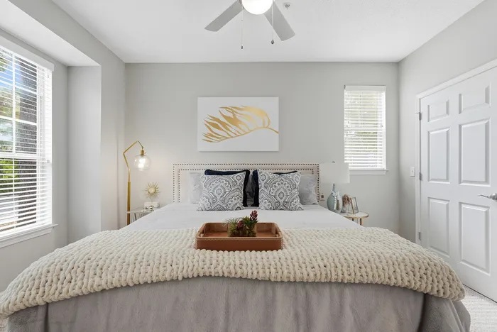 Elegant bedroom with stylish decor, featuring a large bed with plush pillows and a cozy knitted blanket, enhanced by abundant natural light from two windows.