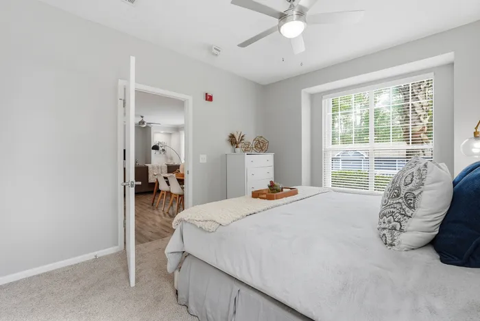 Bright and inviting bedroom with soft carpeting, elegant decor, and a view into a stylishly furnished living area through a wooden door.