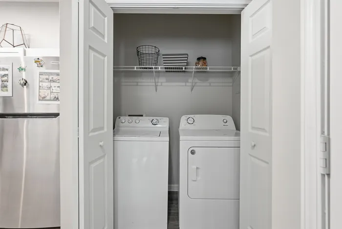 Convenient in-unit laundry space featuring modern washer and dryer, with ample shelving for storage.