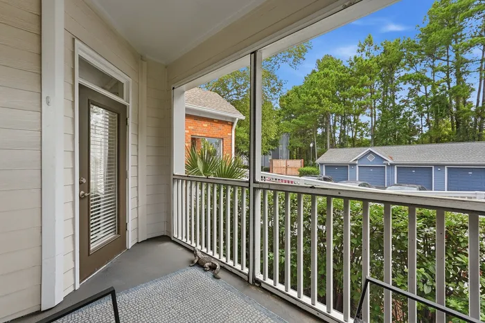 Charming screened porch with serene view of lush greenery and garage, perfect for relaxing moments.