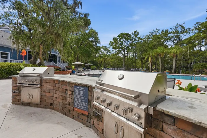 Inviting outdoor area featuring modern stainless steel grills, a sparkling swimming pool, and lush greenery, perfect for relaxed gatherings and entertaining.