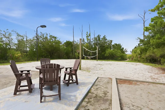 Inviting outdoor space with a beach volleyball court and rustic wooden seating, surrounded by lush greenery under a clear blue sky.