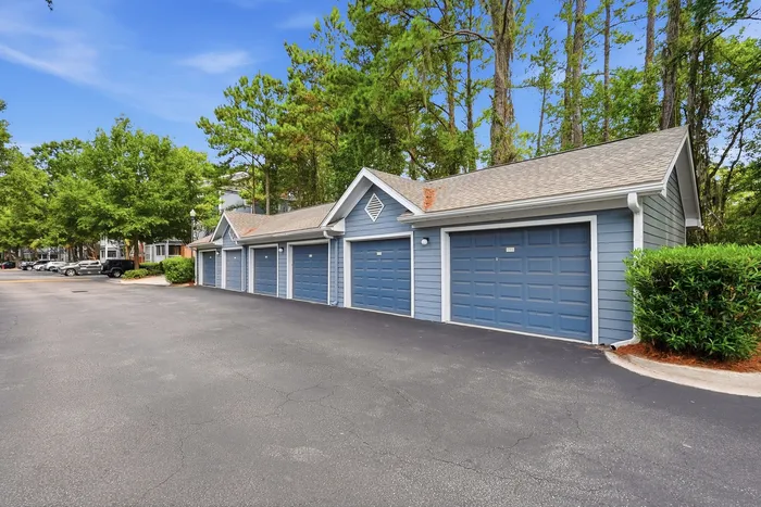 Charming residential area with blue garage units and lush green trees under a bright blue sky, offering ample parking space and serenity.