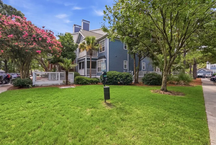 Charming apartment exterior with lush green landscaping and a stunning flowering tree beside a modern, blue-clad building.
