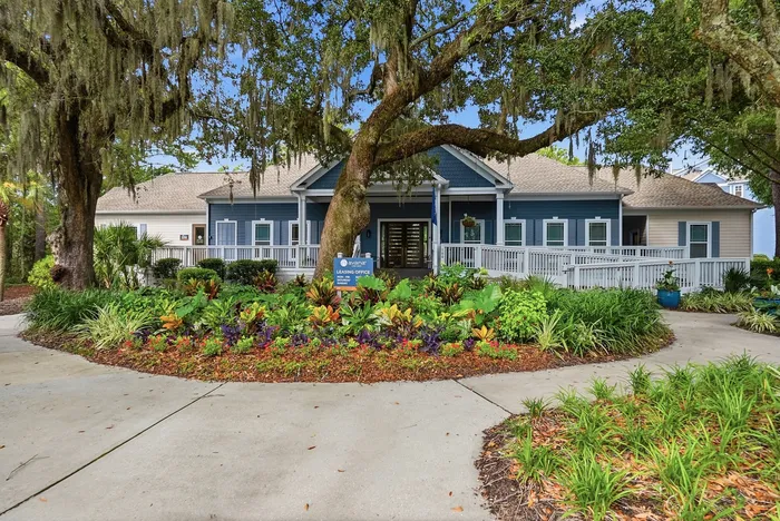Charming leasing office with inviting porch, surrounded by lush landscaping and mature trees, offering a welcoming atmosphere.