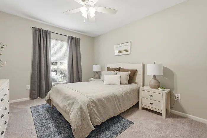 Bright and cozy bedroom featuring a plush queen bed, elegant bedside lamps, and soft gray curtains framing a sunlit window.