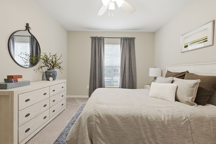 Inviting bedroom with elegant neutral tones, featuring a comfortable bed, stylish mirror, and abundant natural light from a large window.