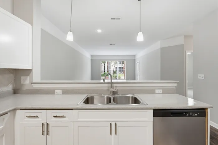 Bright, modern kitchen with double sink, sleek countertops, and pendant lighting overlooking a spacious living area.