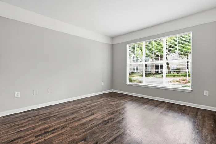 Bright and airy room with large window offering serene garden views, featuring elegant wood flooring and freshly painted walls.