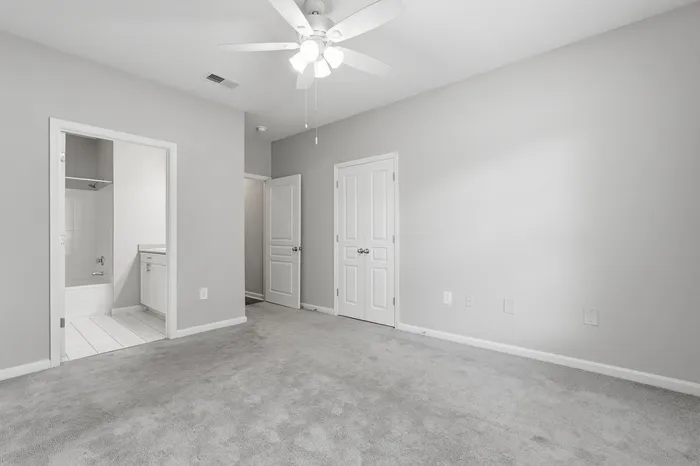 Bright and spacious bedroom featuring plush carpet and ceiling fan, adjacent to a modern en-suite bathroom.