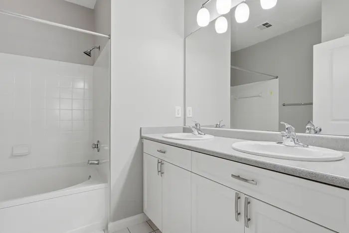 Modern bathroom with elegant dual sinks, sleek countertop, and bright lighting, complemented by a pristine bathtub and stylish fixtures.