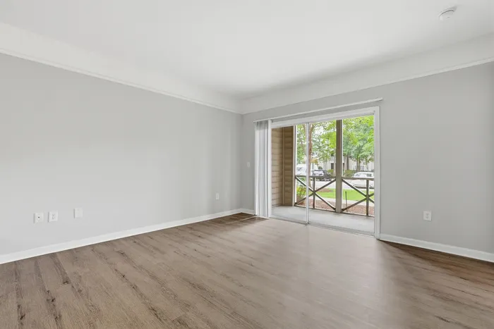 Bright, spacious living room with elegant hardwood floors and a large sliding glass door leading to a serene outdoor view.