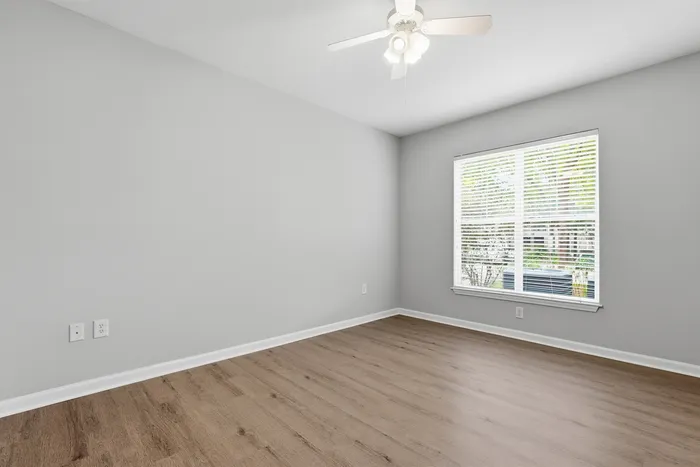 Bright and airy room with elegant wood flooring and a large window, perfect for transforming into a cozy bedroom or stylish home office.