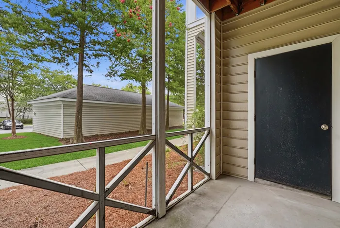 Inviting apartment patio with wooden railing and scenic view of lush green trees and well-maintained pathway.