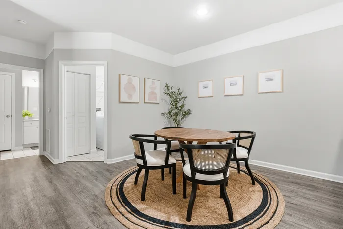 Elegant dining area featuring a round wooden table with stylish chairs, complemented by modern artwork and a cozy rug on a sleek wooden floor.
