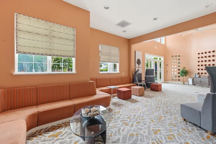 Spacious and modern lounge area featuring stylish orange seating, artistic decor, and ample natural light through large windows.