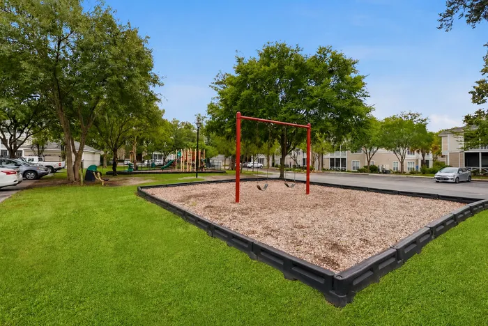 Charming playground with swings set against lush greenery and modern apartment buildings.