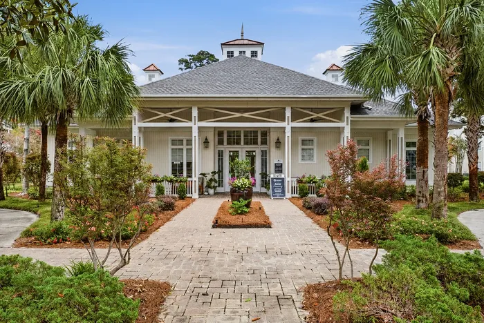 Charming residential entrance featuring a beautifully landscaped pathway leading to a welcoming porch under a stylish roof, surrounded by lush palm trees.