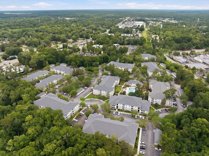Aerial view of modern apartment complex nestled amidst lush greenery, showcasing spacious living with a pool and convenient parking.