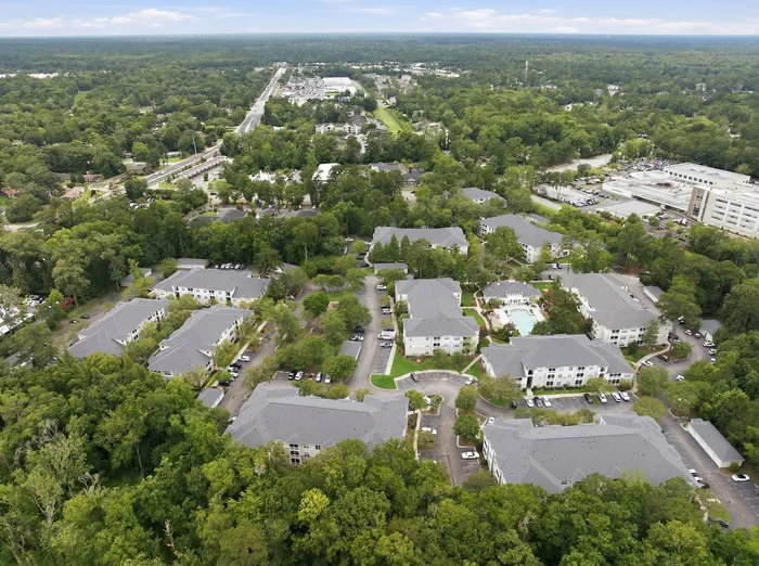 Charming aerial view of modern apartment complex nestled in lush greenery, featuring elegant architecture and a spacious swimming pool.