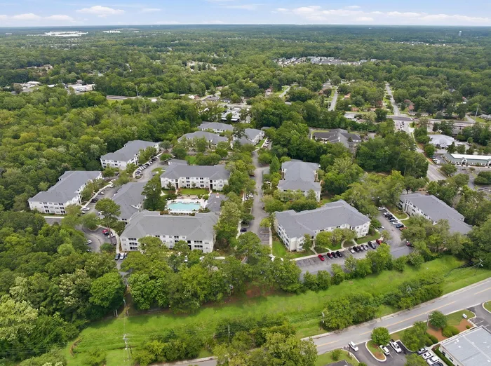 Stunning aerial view of a serene apartment complex surrounded by lush greenery, featuring multiple residential buildings and a central pool area.